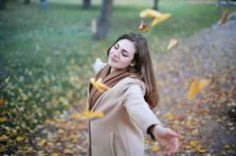 Une femme adulte avec les bras écartés respirant l'air dans un jardin en automne.